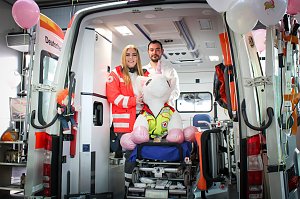 Ein geöffneter Rettungswagen steht im Autohaus. Zwei Mitarbeitende des Deutschen Roten Kreuzes stehen darin, vor ihnen sitzt ein großes Stoff-Einhorn auf einer Krankentrage. Rosa Luftballons schmücken den Wagen.