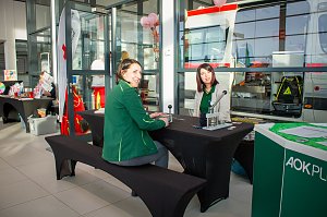 Zwei Frauen sitzen an einem schwarzen Tisch mit Infomaterial. Im Hintergrund steht ein Rettungswagen. Auf dem Tisch liegen Geräte, vermutlich für eine Mitmachaktion. Rechts ist ein grüner Stand der AOK Plus zu sehen.