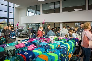Viele Besucher stehen an Tischen voller bunter Schulranzen. Im Hintergrund ist ein schwarzes Škoda-Fahrzeug ausgestellt, rosa Flamingos hängen von der Decke.