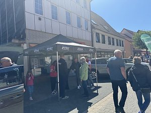 Menschen unterhalten sich unter einem schwarzen Autohaus Peter-Pavillon, daneben ein graues Ausstellungsfahrzeug.
