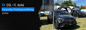 Veranstaltungsbanner und Fahrzeugpräsentation: Schwarzes Banner mit Text „09.11. Mai, Gewerbe-Fachausstellung Zerbst“ neben einem ausgestellten grauen Mercedes-Benz SUV vor dem Stand der Autohaus Peter Gruppe.