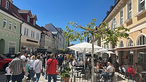 Belebte Fußgängerzone in Heiligenstadt bei sonnigem Wetter. Zahlreiche Menschen schlendern zwischen den farbigen Altstadthäusern, im Vordergrund Cafétische mit Sonnenschirmen.