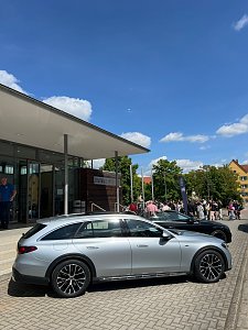 Vor der Stadthalle Wittenberg steht ein silberner Mercedes-Benz Kombi. Im Hintergrund sind weitere Autos, Menschen und eine Mercedes-Fahne zu sehen.