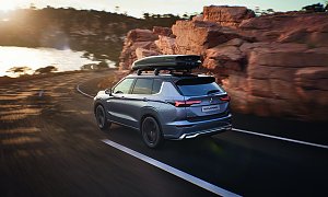 Mit Dachbox: Mitsubishi Outlander von hinten auf einer Küstenstraße, mit montierter Dachbox, umgeben von Felsen und Blick auf das Meer.