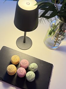 Schwarze Servierplatte mit sechs bunten Macarons, alle mit Aufdruck She’s Mercedes, daneben Tischlampe und Blumenvase.