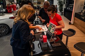 Mehrere Frauen betrachten eine Duftauswahl an einem Ladies Special-Stand, eine Frau trägt ein rotes Shirt.eine Frau trägt ein rotes Shirt und hält ein Glas Rosé.