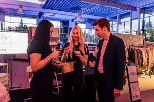 Drei Personen, darunter Christina Dost, ziehen Lose aus einem goldenen Hut, zwei halten Mikrofone, im Hintergrund ein Bildschirm mit She’s Mercedes Ladies Night und Kleidungsständer.
