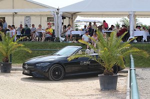 Ein schwarzes Mercedes-Benz Cabrio steht am Rand des Sandplatzes beim Reitturnier in Immenrode, flankiert von zwei Palmen im Topf. Im Hintergrund sitzen Zuschauer unter weißen Eventzelten an Tischen.