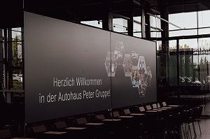 Leinwand mit der Begrüßung ‚Herzlich willkommen in der Autohaus Peter Gruppe!‘ in der Firmenzentrale in Nordhausen. Auf der Leinwand sind auch Fotos von Mitarbeitern und Azubis zu sehen.