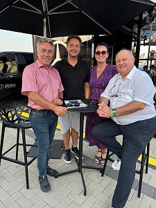 Gruppenfoto am Mercedes Cube: Centerleiter Marko Wuttke, Geschäftsführer Alexander Kästner, Geschäftsführerin Christina Dost und Seniorchef Helmut Peter stehen bzw. sitzen um einen Stehtisch unter einem Sonnenschirm. Auf dem Tisch liegen Prospekte und ein Modellauto.