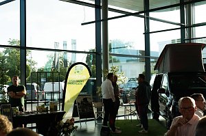 Ein Messestand mit gelb-grünem Banner Möbius – Grün macht glücklich!. Daneben ein schwarzer Mercedes-Camper mit hochgeklapptem Dach. Zwei Männer und weitere Personen unterhalten sich.
