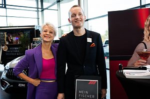 Eine Frau (Moderatorin Mandy Kossira) in lila Blazer und pinkem Top steht neben einem Mann im schwarzen Anzug. Beide lächeln. Neben ihnen ein Aufsteller mit der Aufschrift Mein Fischer.