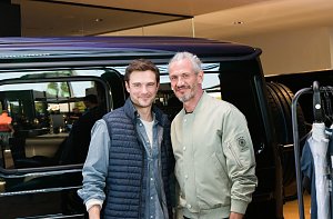 Zwei Männermodels stehen nebeneinander vor einem schwarzen Mercedes. Beide lächeln in die Kamera, einer trägt eine helle Bomberjacke, der andere eine dunkle Weste.
