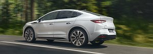 Skoda Enyaq Coupé in weiß fährt schnell auf einer Straße im Wald