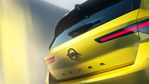 Nahaufnahme des gelben Fahrzeugs von hinten. Sichtbar sind die markanten, schmalen LED-Rückleuchten, das Opel-Logo in der Mitte der Heckklappe und der Schriftzug ASTRA. Die Heckscheibe mit Spoiler und Scheibenwischer ragt über den oberen Bereich. Die Beleuchtung und leichte Unschärfe erzeugen einen futuristischen Eindruck.