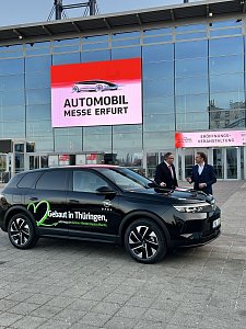 Schwarzer Opel-SUV vor der Messe Erfurt, im Hintergrund LED-Schild Automobil Messe Erfurt, zwei Männer im Gespräch.