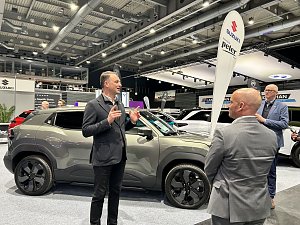 Andreas Peter erklärt einen grauen SUV am Messestand, zwei Zuhörer stehen davor. Im Hintergrund Suzuki-Banner und weitere Autos.