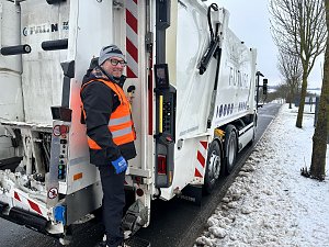 Verkaufsberater vom Autohaus Peter André Schmidt steht auf der Trittstufe eines Müllfahrzeugs während der Fahrt durch ein Industriegebiet.