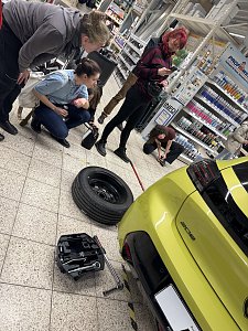 3 Frauen stehen neben einem gelben Peugeot 208, auf dem Fußboden liegt ein Rad