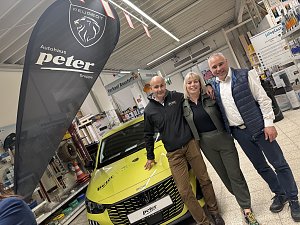 2 Männer und eine Frau neben einem gelben Peugeot im Baumarkt; daneben schwarze Autohaus Peter Beachflag