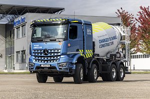 Elektrischer Betonmischer Mercedes-Benz eArocs 400 steht vor einem modernen Firmengeb&auml;ude mit B&auml;umen im Hintergrund
