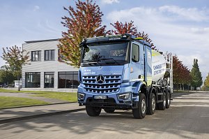 Elektrischer Betonmischer Mercedes-Benz eArocs 400 f&auml;hrt auf einer Stra&szlig;e vor einem modernen Geb&auml;ude