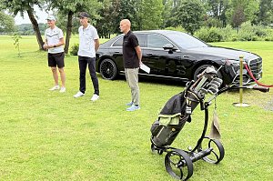 Turnierleitung begrüßt die Teilnehmenden auf dem Golfplatz vor einer schwarzen Mercedes-Benz Limousine.
