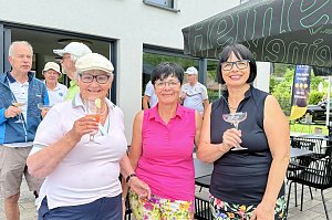 Drei Golferinnen posieren mit Getränken vor dem Clubhaus während der Veranstaltung.