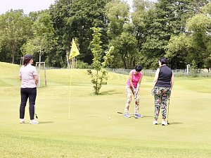 Drei Golferinnen auf dem Grün beim Putten in sommerlicher Atmosphäre.
