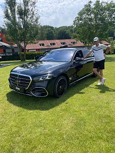 Golfspieler lehnt an einer schwarzen Mercedes-Benz Luxuslimousine auf dem Veranstaltungsgelände.