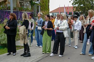 Eine größere Gruppe von Frauen, die im Freien auf einem Gehweg stehen und gemeinsam aufmerksam in eine Richtung blicken.