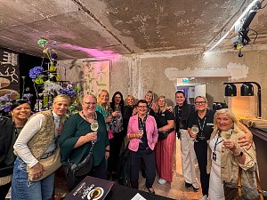 Eine Gruppe von Frauen, die mit Getränken in den Händen in einem rustikalen Innenraum für ein gemeinsames Foto posieren.