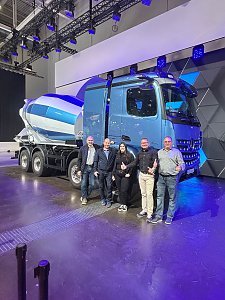 Fünf Personen stehen lächelnd nebeneinander vor einem hellblauen Mercedes-Benz Betonmischer auf einer Messebühne. Die große Mischtrommel hinten ist weiß-blau gestreift.