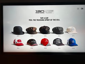Digitaler Bildschirm zeigt zehn historische und moderne Kopfbedeckungen in zwei Reihen. Oben steht das Logo 130 YEARS TRUCKS und die Aufforderung TAP A CAP. FEEL THE TRUCKING SPIRIT OF THE ERA.