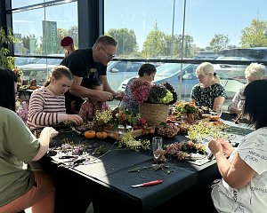 Erwachsene und Kinder sitzen an einer gro&szlig;en Tafel und binden aus Hortensien, Zweigen und weiteren Naturmaterialien herbstliche Kr&auml;nze.