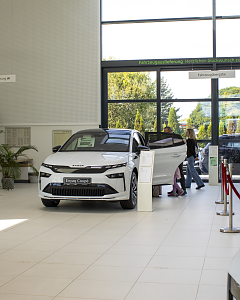 Ein wei&szlig;er �koda Enyaq Coup&eacute; steht im hellen Showroom der Autowelt Peter. Im Hintergrund betrachten Besucher weitere Fahrzeuge.