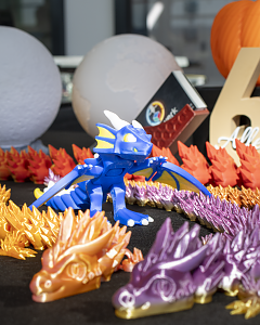Bunte gedruckte Drachenfiguren in Blau, Orange und Violett auf einem Ausstellungstisch.