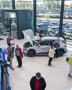 Besucher informieren sich im �koda-Autohaus &uuml;ber ein wei&szlig;es Fahrzeug mit ge&ouml;ffneter Motorhaube und weiteren ausgestellten Modellen im Hintergrund.