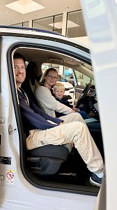 Familie mit Kind sitzt gemeinsam in einem wei&szlig;en �koda und testet den Innenraum des Fahrzeugs im Autohaus.