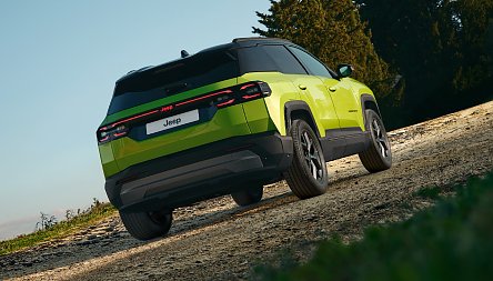 Der neue Jeep® Compass e-Hybrid - Grüner Jeep Compass von hinten, fährt leicht bergauf auf einem Schotterweg, Bäume im Hintergrund.