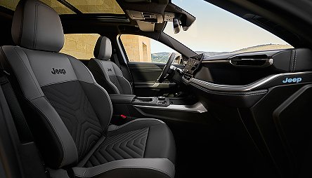 Der neue Jeep® Compass e-Hybrid - Innenraum des Jeep Compass mit schwarzen Sitzen, modernem Cockpit und großem Panoramadach, Sicht nach draußen.