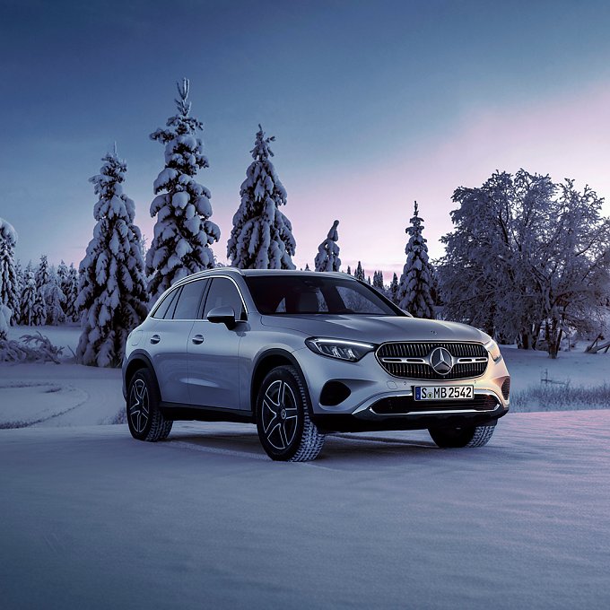 Mercedes-Benz GLC steht in verschneiter Winterlandschaft mit schneebedeckten Tannen, aufgenommen in ruhiger Abenddämmerung.