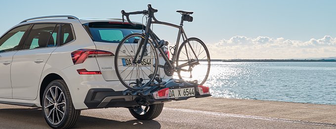 Wei&szlig;er Kombi mit zwei Fahrr&auml;dern auf Hecktr&auml;ger am Wasser geparkt.